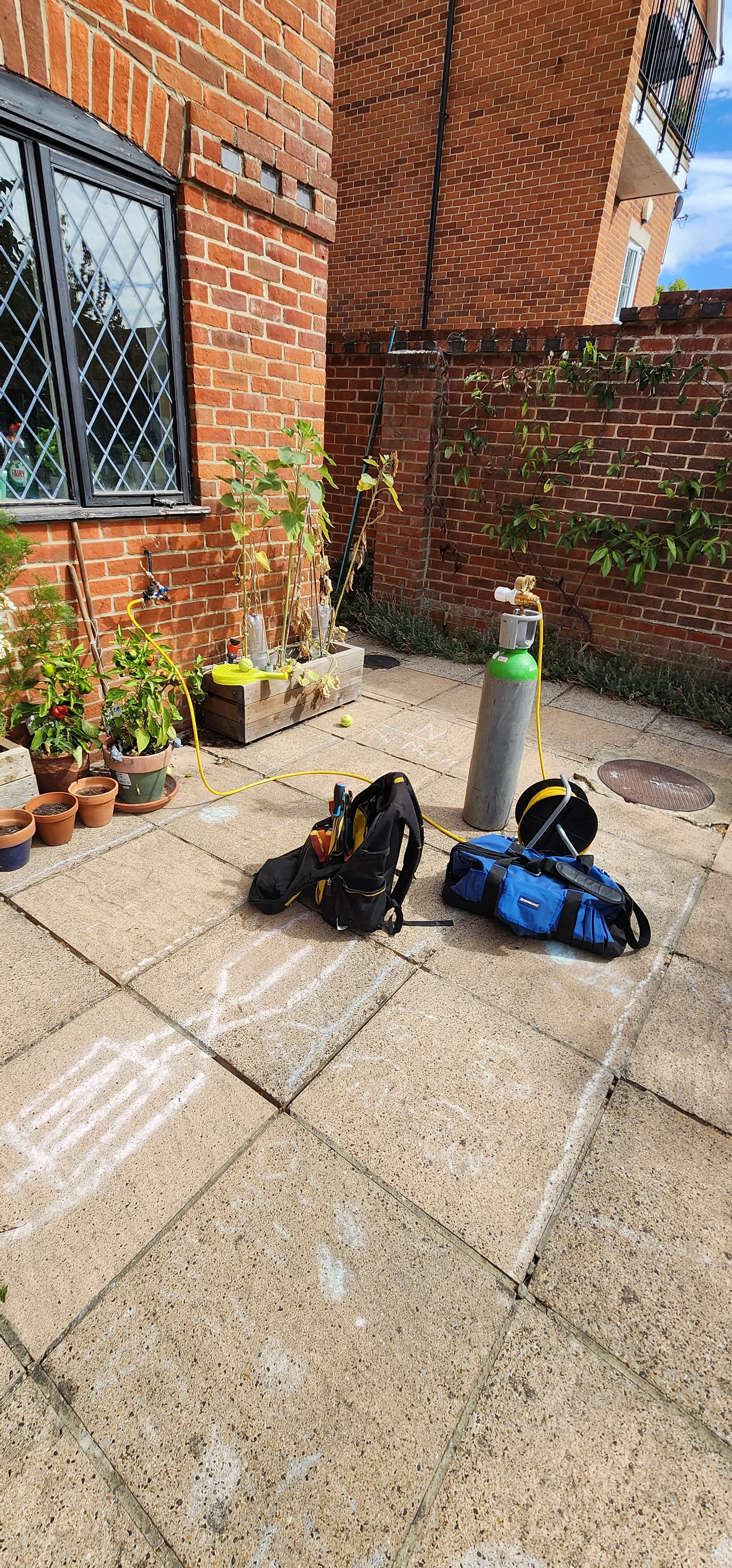 Gas cylinder, hose and investigation equipment arranged on a paved area outside a brick property