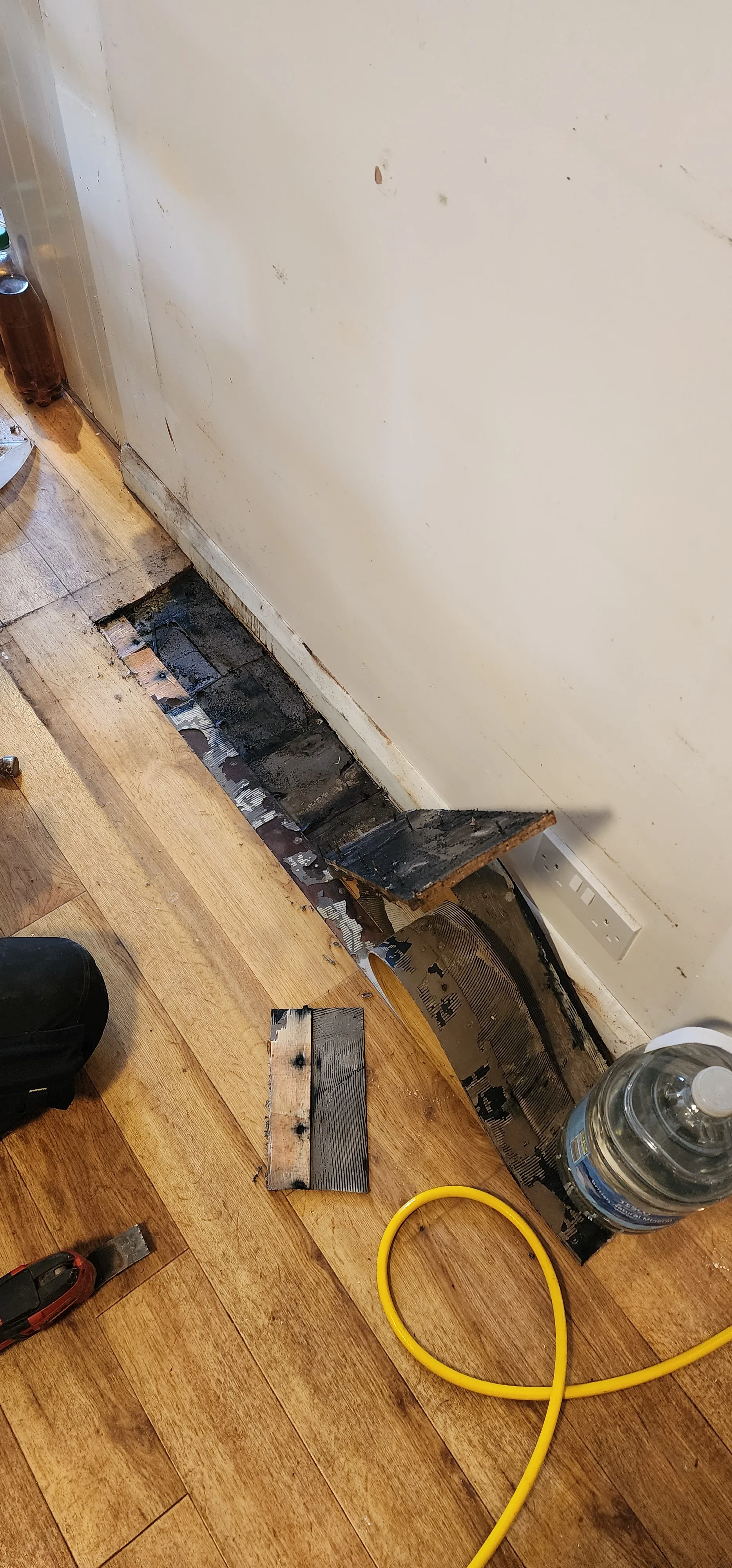Narrow opened section of timber kitchen flooring beside a wall