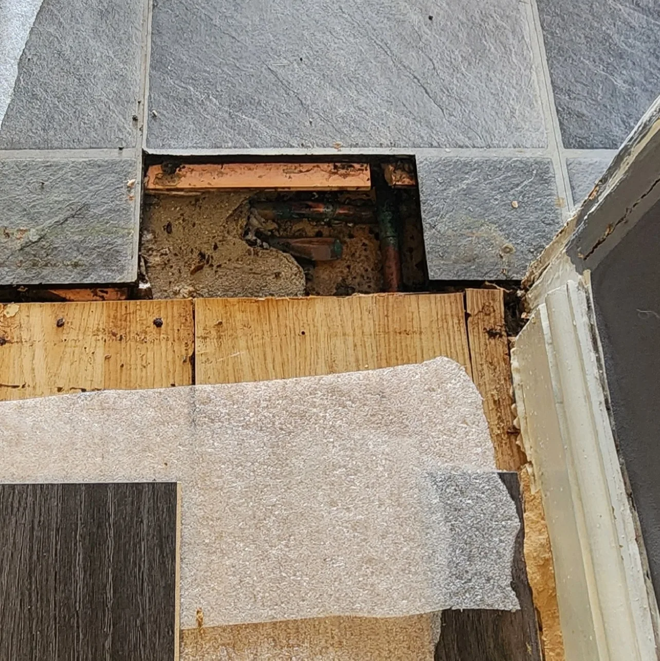 Copper pipework visible through a small opening in the tiled kitchen floor