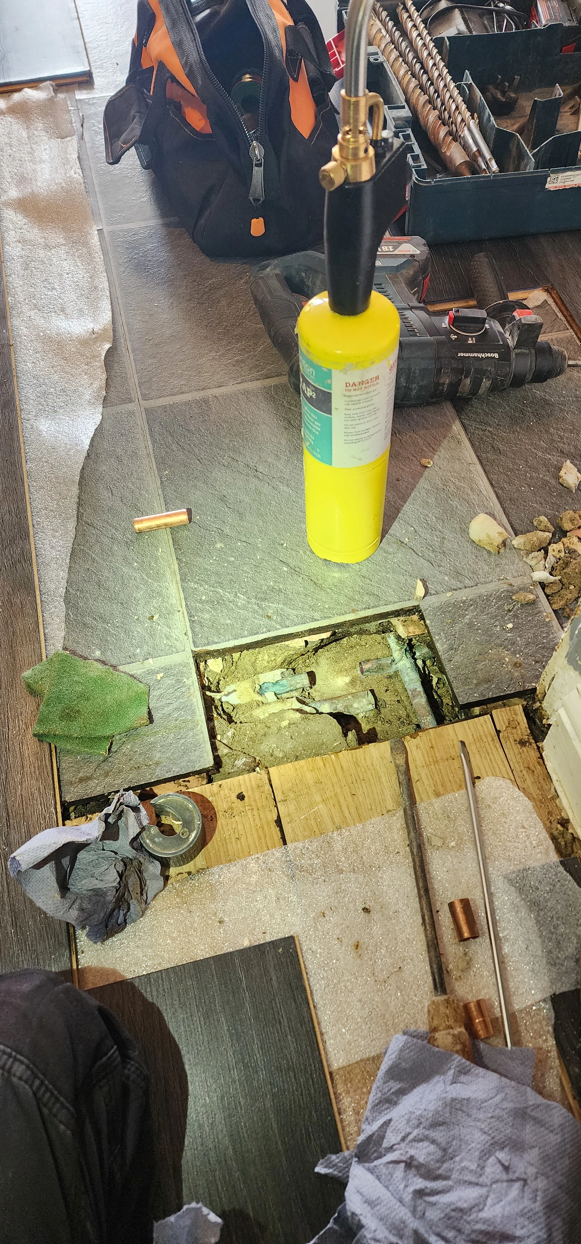 Opened kitchen floor with exposed copper pipework and repair tools